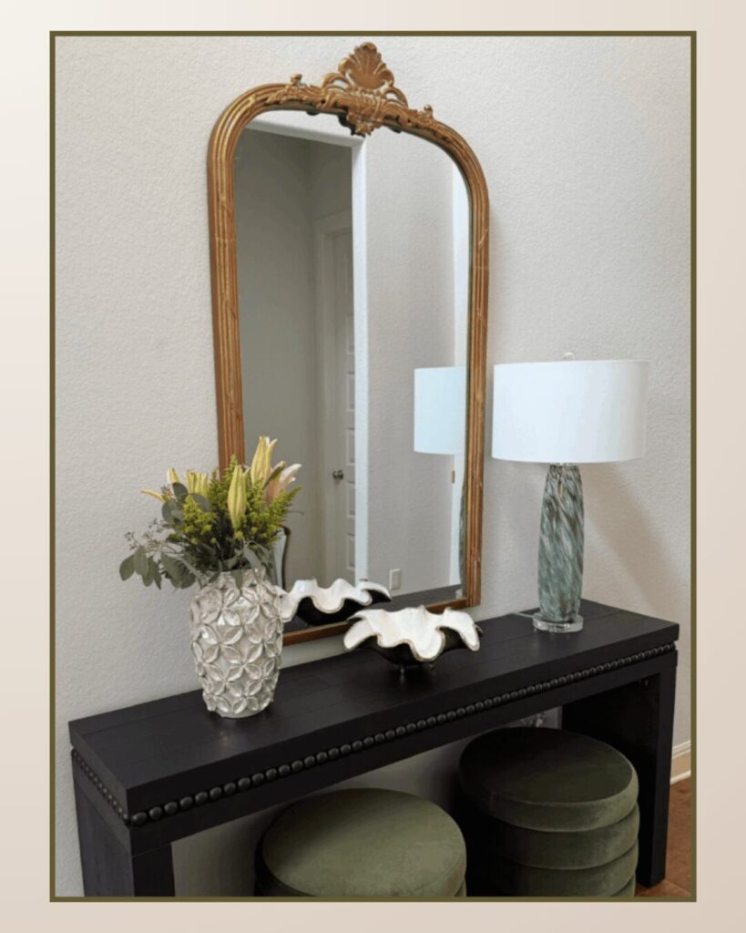 Elegant black console table with a decorative mirror above, featuring a vase of flowers, a sculptural accent, and a stylish lamp.
