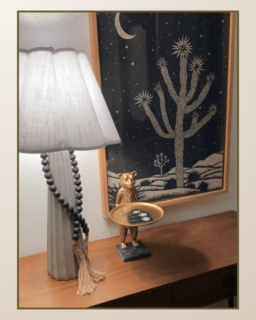 Warm lamp and a decorative bear figurine holding a dish, set against a starry desert landscape artwork. Stylish and cozy arrangement.