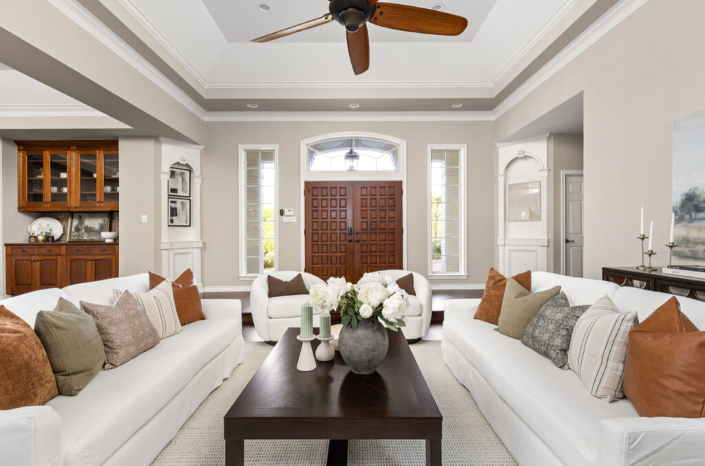 Bright living room with white sofas adorned with colorful pillows, a dark wooden coffee table, and a beautifully detailed front door.