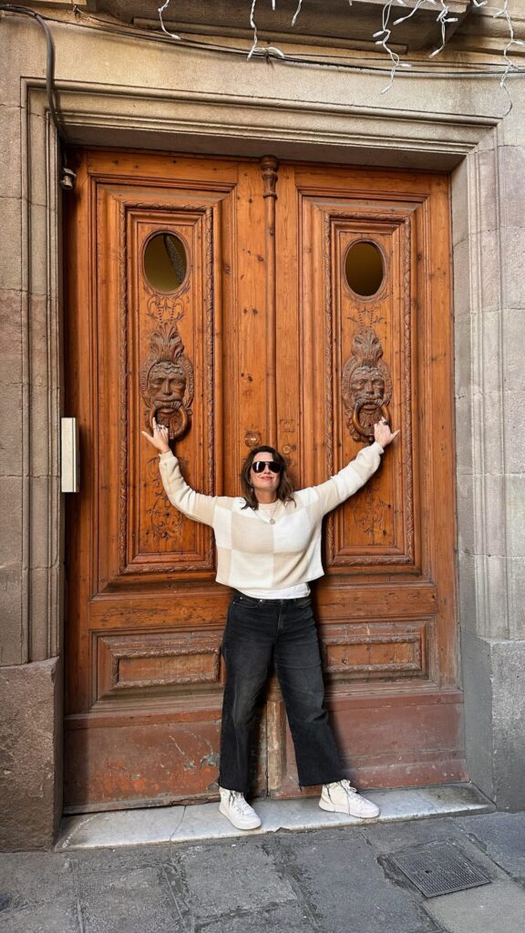 A person in a striped sweater and sunglasses stands in front of large, intricately carved wooden doors, showcasing warm brown tones.