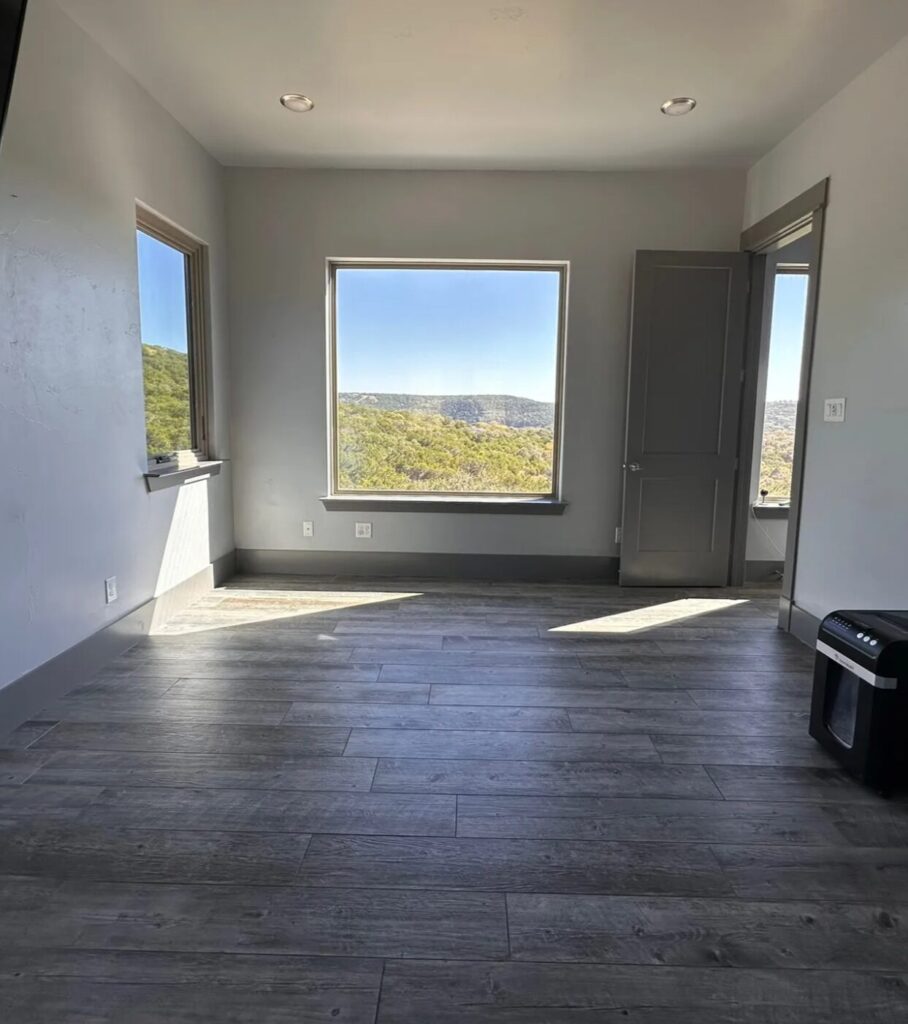 Bright, empty room featuring gray walls, large window with scenic views, and hardwood flooring, ready for a cozy reading nook.