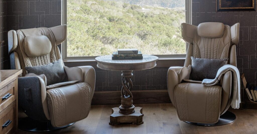 Cozy neutral-toned chairs with high backs facing a window, accompanied by a round table, set in a nature-inspired interior.