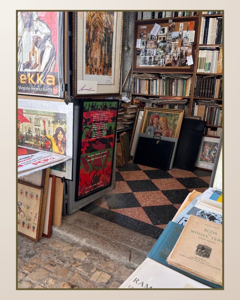 A cozy corner of a bookshop featuring colorful art posters, framed paintings, and stacks of books on a patterned floor.