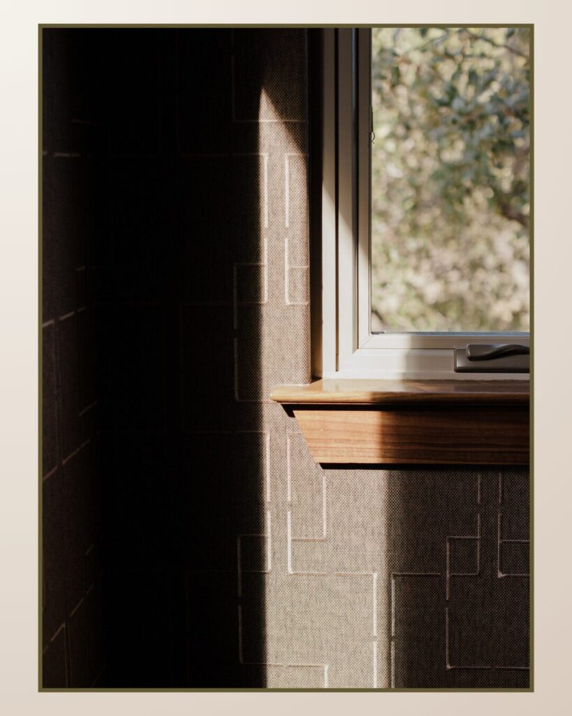 Natural light streams through a window, casting soft shadows on a textured wall with geometric patterns and a wooden ledge.