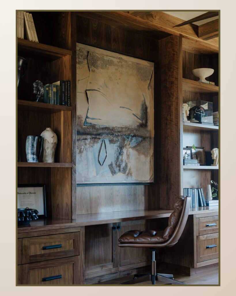 Elegant study with wood shelves displaying art and books, a textured painting as the focal point, and a stylish brown leather chair.