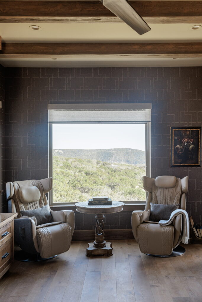 Modern reading nook featuring two stylish beige armchairs, a round coffee table, and large window with scenic views of greenery outdoors.