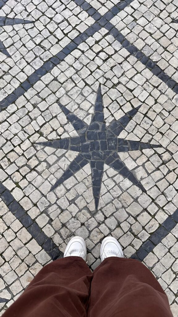 Cobblestone pavement featuring a star design, viewed from above with white shoes and brown pants in the foreground.