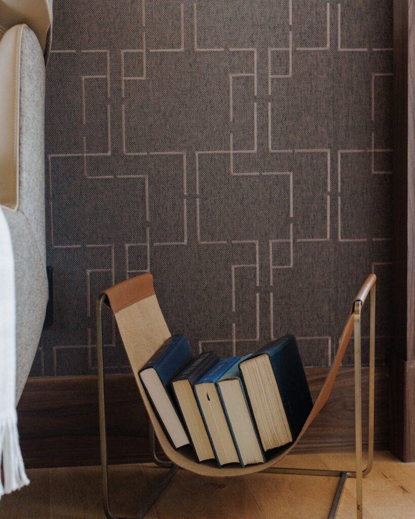 A stylish book holder with several books rests against a textured, patterned wall in a modern interior setting.