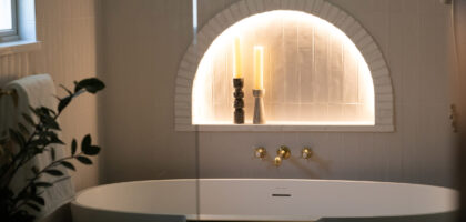 Elegant bathroom featuring a freestanding white tub, golden fixtures, and an arched alcove with candles and decorative objects.
