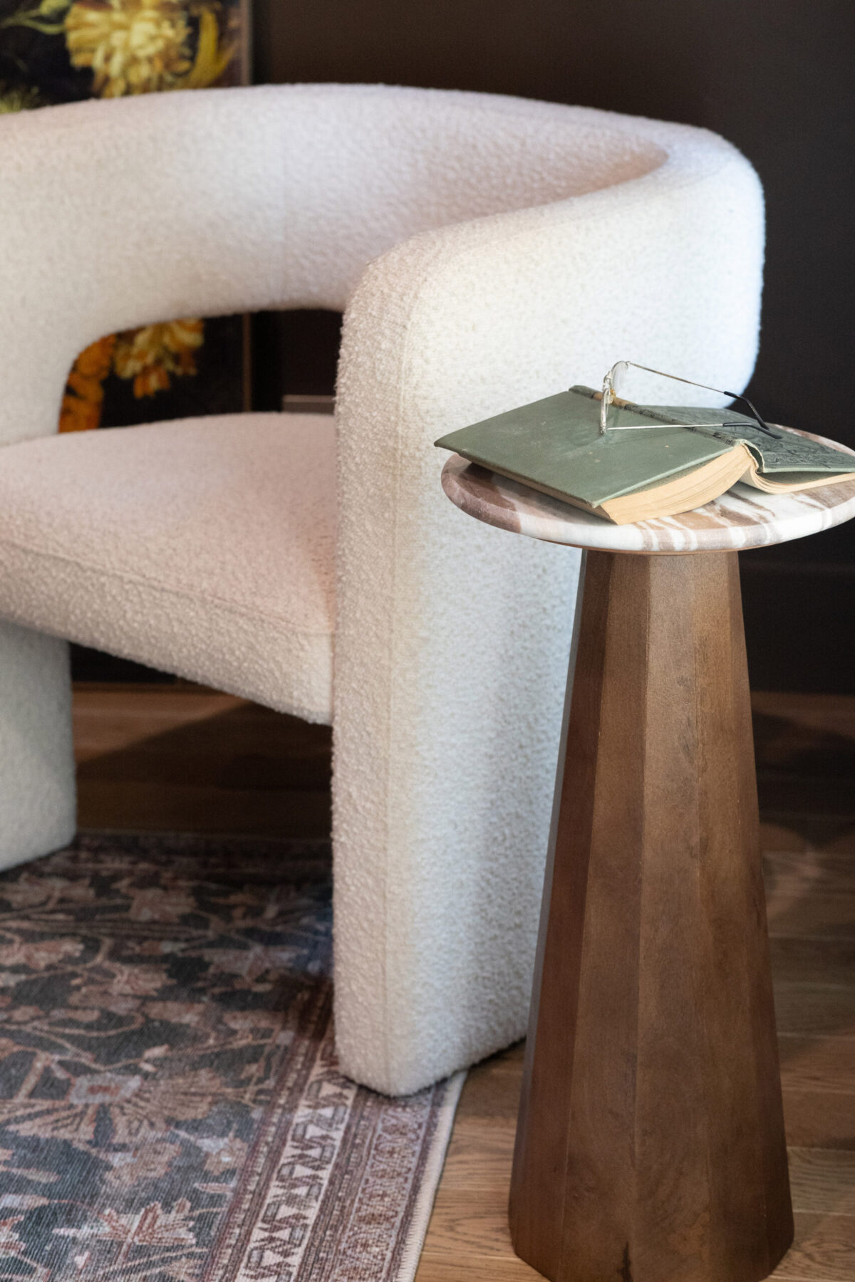 Textured white chair beside a sleek wooden side table, featuring a green book and a metal bookmark on a patterned area rug.