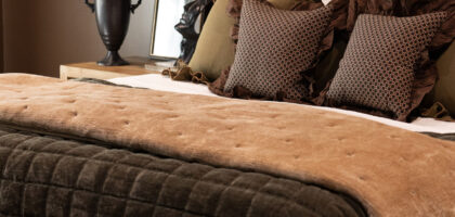 Cozy bedroom featuring a wooden bed with layered bedding in earthy tones, decorative pillows, a stylish bedside lamp, and a floral arrangement.