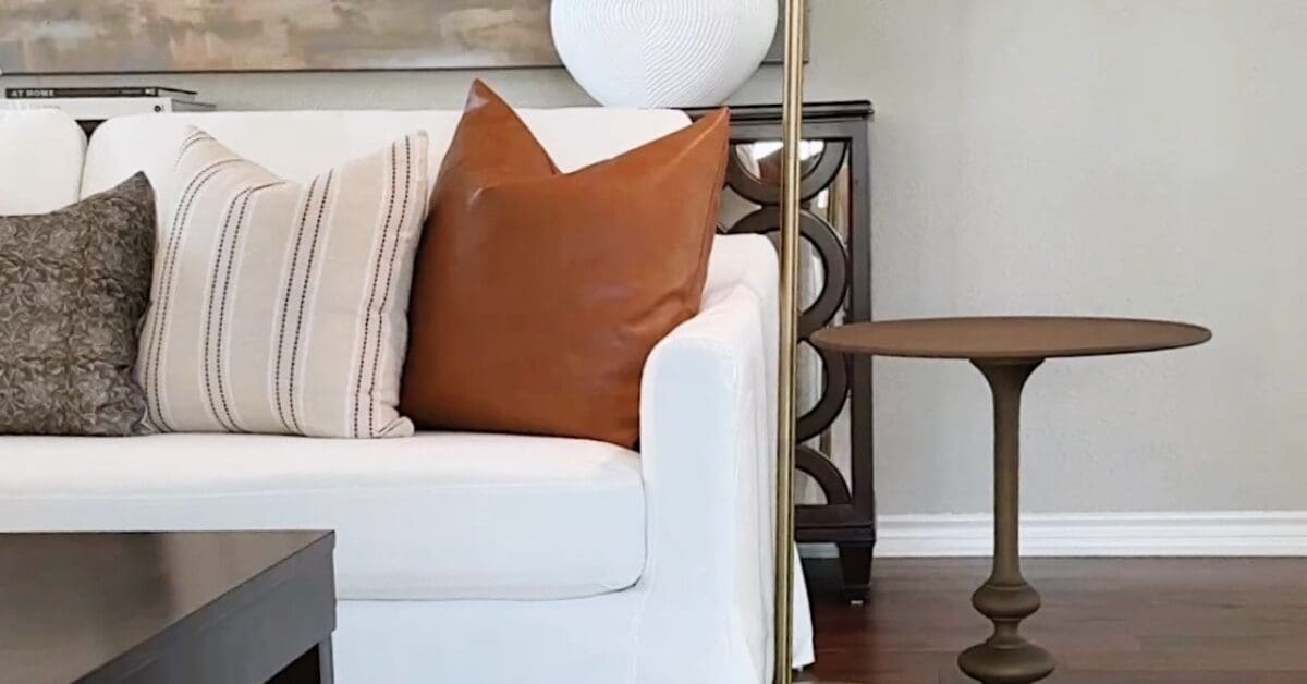 a white couch in the living room with throw pillows (orange, white with stripes, and brown) with a brown side table